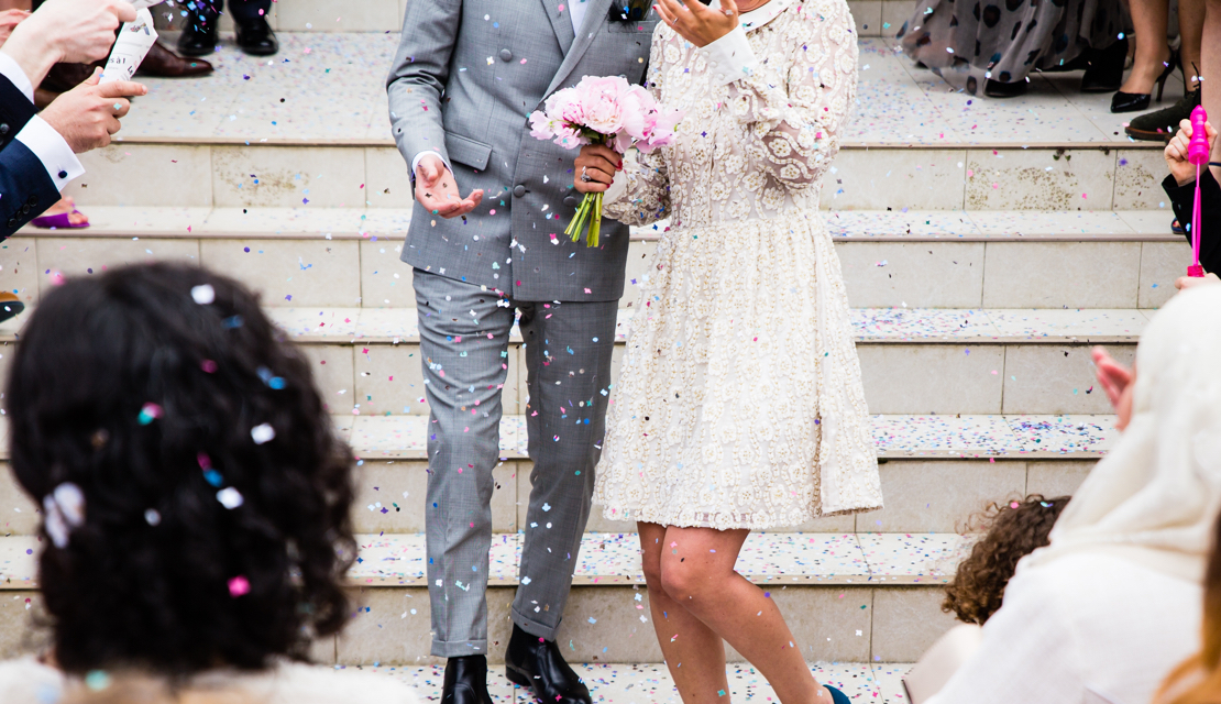 Brautpaar auf Treppe mit Konfetti und Gästen umringt