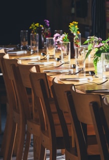 Eingedeckter Holztisch mit Blumen, Tellern, Besteck, Gläsern und Holzstühlen