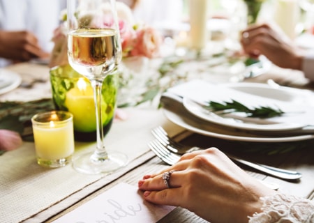 Frauenhand auf festlich gedecktem Tisch mit Sektglase, Kerzen, Tellern und Besteck